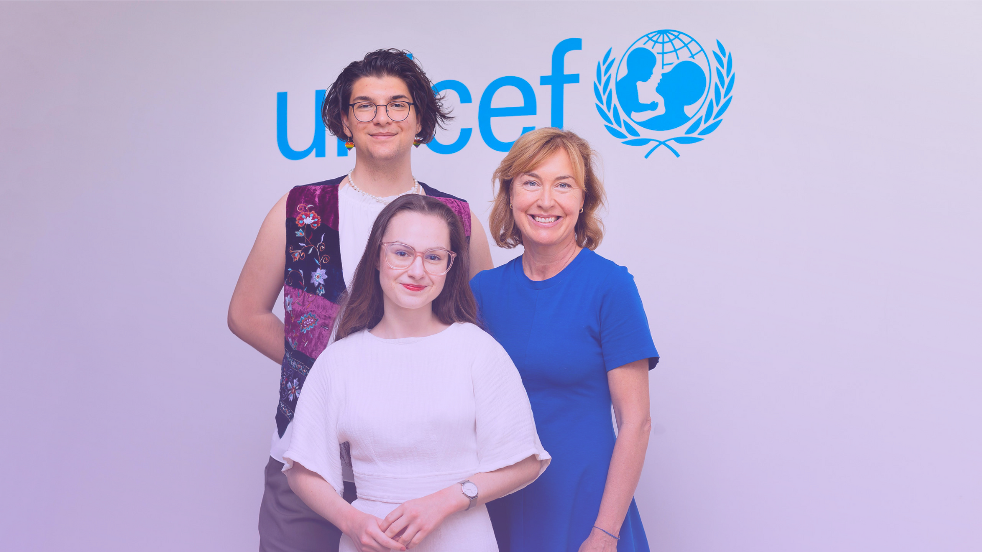 Foto på Elias Fjellander, Pernilla Baralt och Lilian Helgason framför en vit vägg med UNICEF:s logga i blått. Alla tittar in i kameran och ler.
