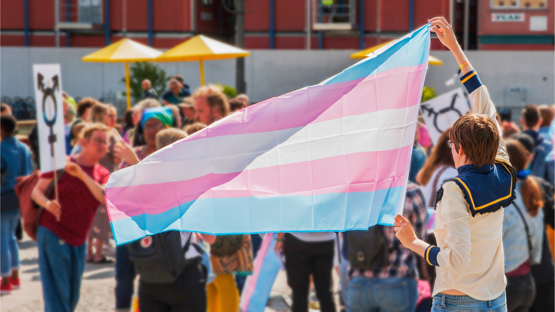Foto från transdemo 2019. En person i en sjömanskjorta som håller upp transflaggan på en demonstration.