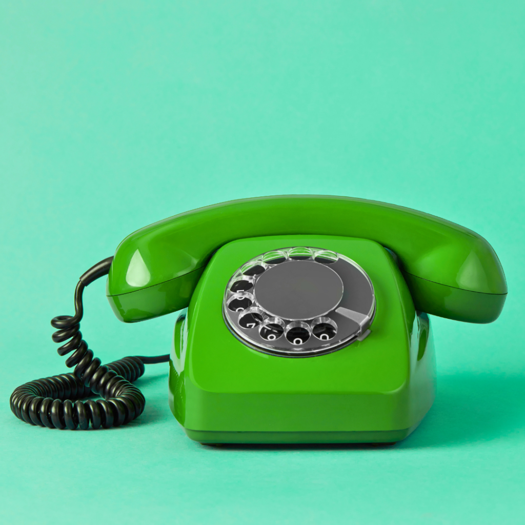 Foto på en stationär grön telefon med snurrskiva mot en turkos bakgrund.