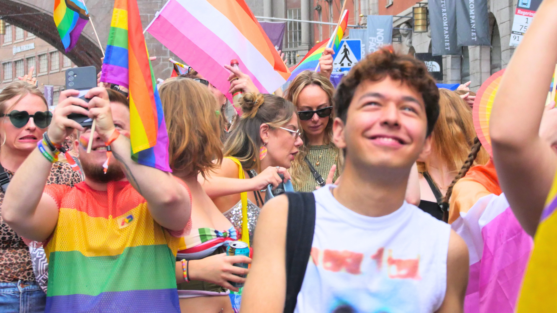 Foto på deltagare i vårt paradblock från Stockholm Pride 2024. Vissa är glada och fotar medan andra gör grimaser och pekar finger. Många viftar med regnbågsflaggor och flaggan för lesbiska.