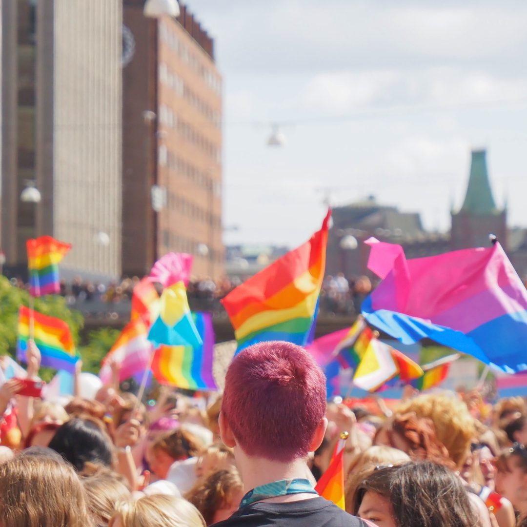 Foto på deltagare i vårt paradblock från Stockholm Pride 2023. Många viftar med regnbågsflaggor: några viftar med flaggan för bisexuella, transpersoner och lesbiska.