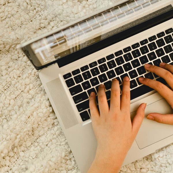 Närbild på två händer på en bärbar dator som står på en vit filt.